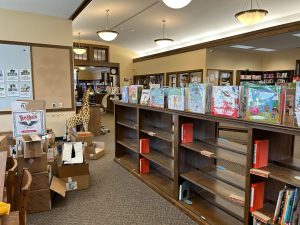 partially emptied bookshelves of picture books with a pile of empty boxes