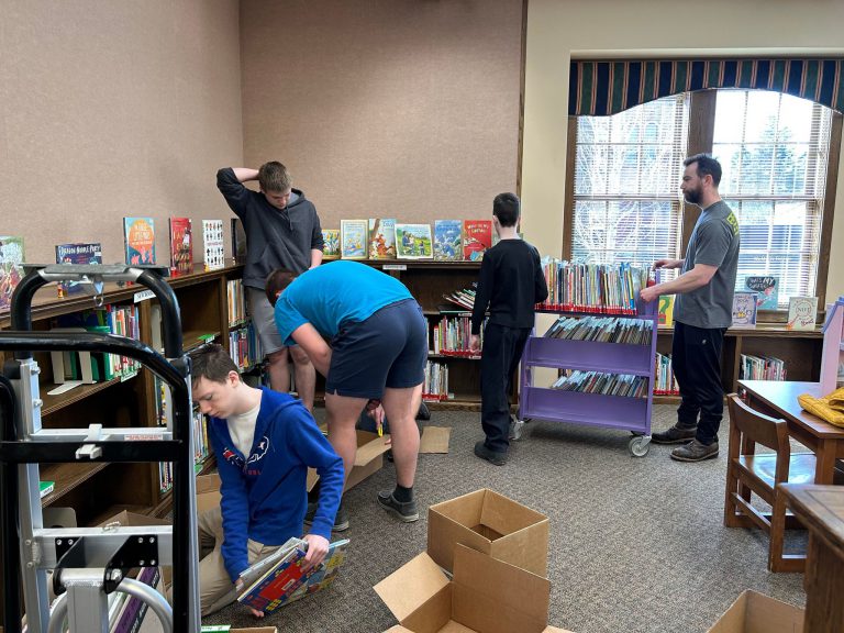 four teen boys and a man load boxes and a book cart with picture books