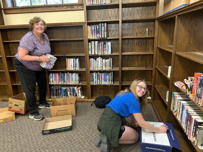 woman and teenage girl smile while packing books into boxes