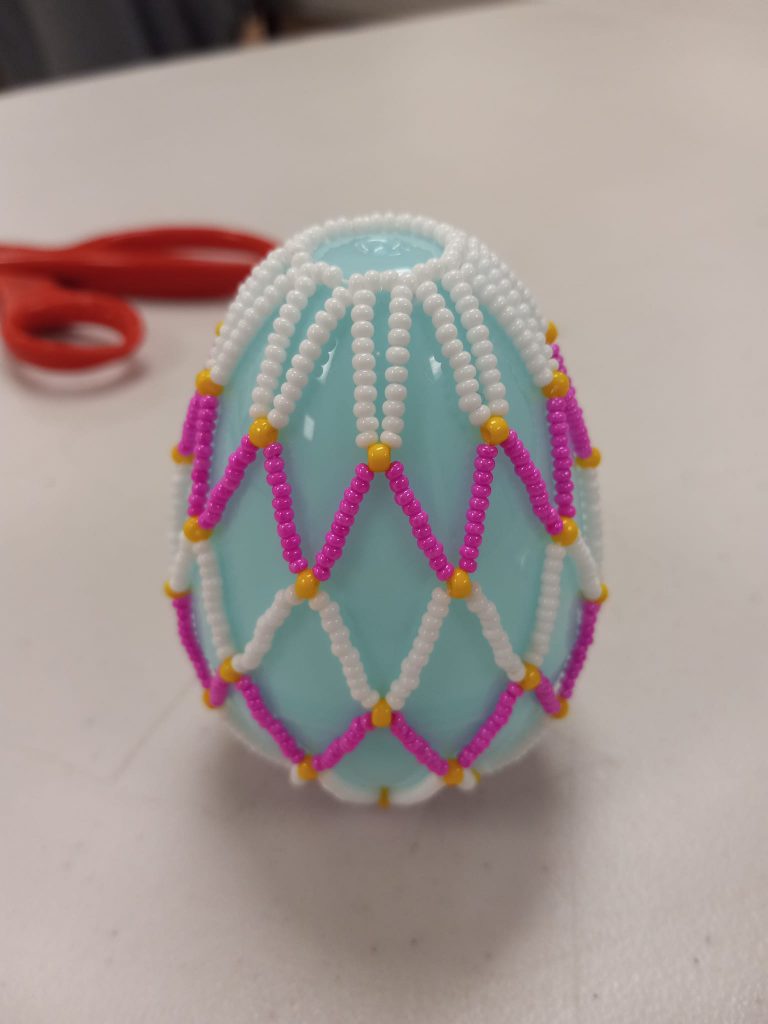 light blue plastic egg with white, pink and yellow beaded net