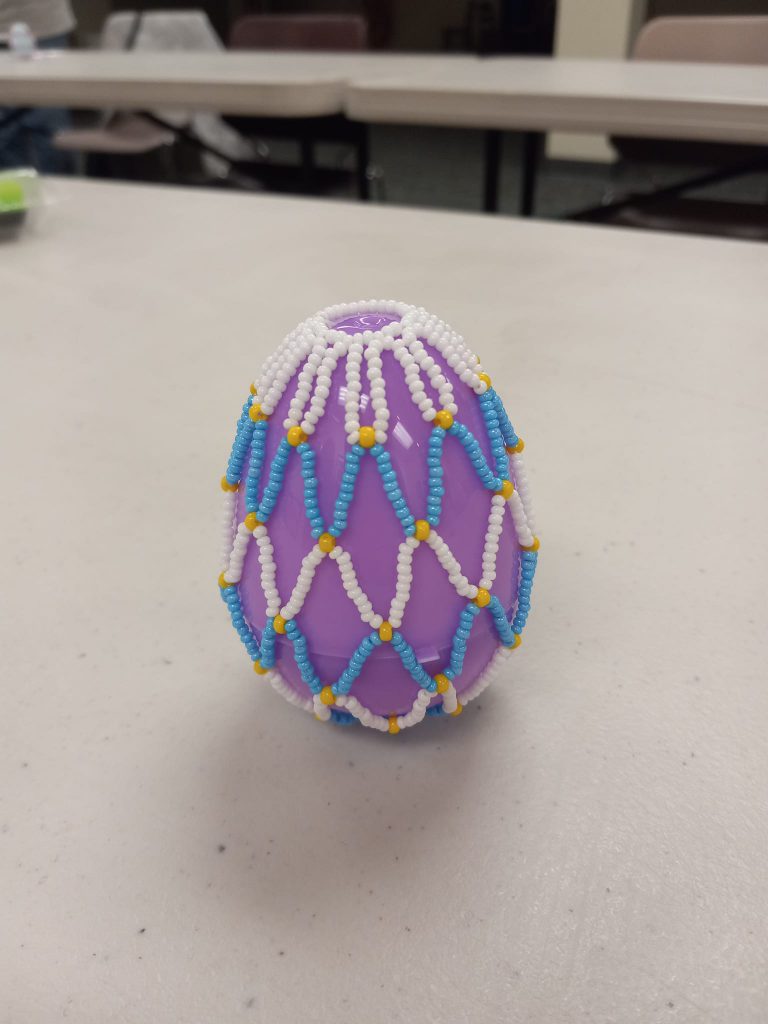 purple plastic egg with white, yellow and blue beaded net