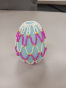 light blue plastic egg with white, yellow, and pink beaded net