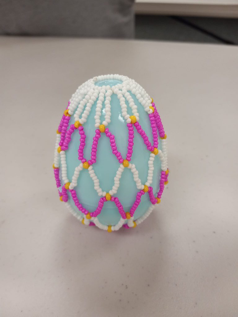 light blue plastic egg with white, yellow, and pink beaded net