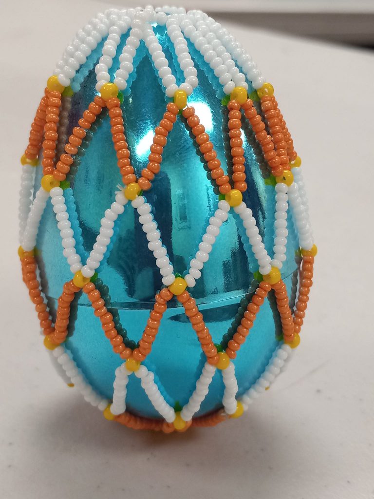 shiny blue plastic egg with white, yellow and orange beaded net