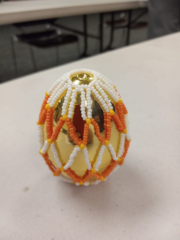 shiny gold plastic egg with white, yellow and orange beaded net