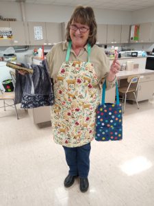 woman with deer apron holds blue polka dot tote bag and grey & blue pillow case