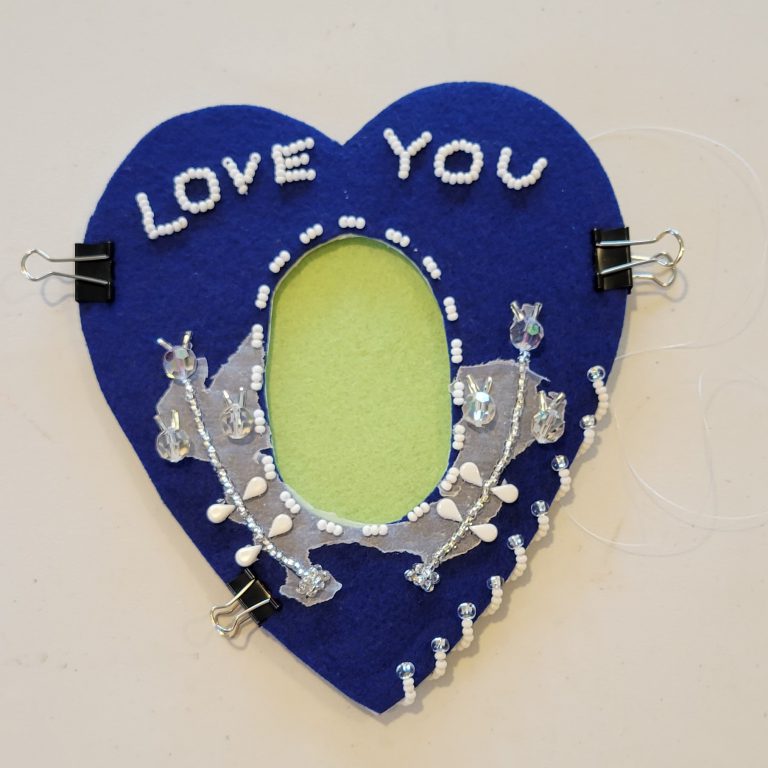 dark blue felt in heart shape with light green felt oval in center and clear and white beaded design