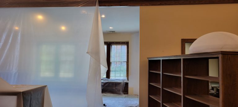 beige wall with bookcase and plastic tarp hanging nearby