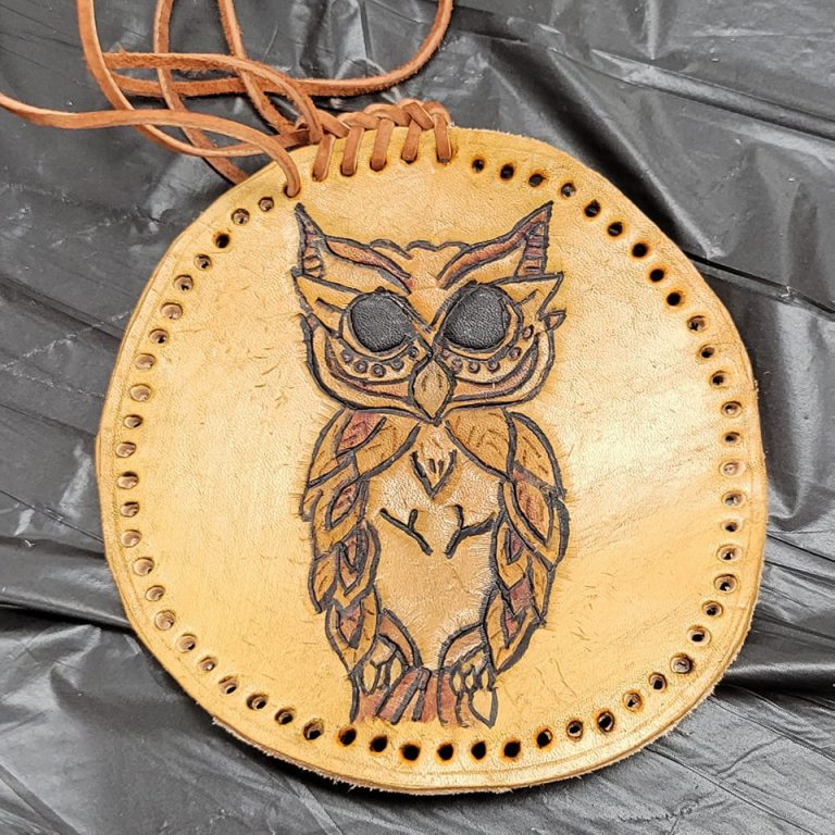 tan circular leather medallion with holes punched for lacing around the rim and image of owl tooled into it