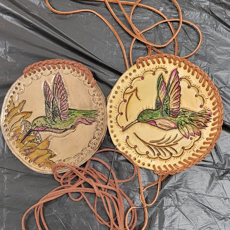 brown and tan circular leather medallions with braided lacing stitched partway around the rim and images of colorful hummingbirds tooled into them