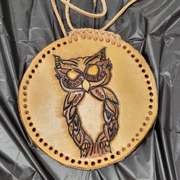 tan circular leather medallion with braided lacing being stitched around the rim and image of owl tooled into it