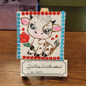 brown and white cartoon cow with red rose and a border of blue and red gems