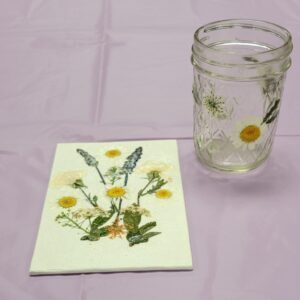 small glass jar and canvas with purple and white pressed flowers and leaves