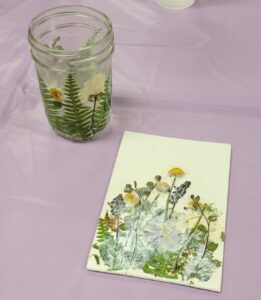 small glass jar with yellow purple and white pressed flowers and leaves