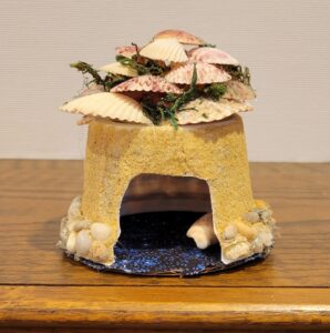 upside down yogurt cup glued to cardboard base with sand walls and shell roof and decor