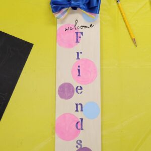 rectangular sign with welcome friends and pink purple and blue polka dots painted on and a blue and plaid bow