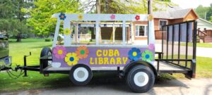 parade float made to look like VW bus with white and purple paint and colorful flowers with Cuba Library lettering