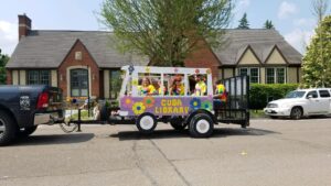 VW bus parade float in front of library building with staff wearing tie dye shirts