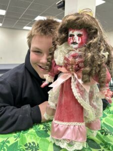 boy with blond hair and black hoodie with doll with bloody face and dress