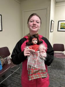 girl with brown hair and red and black shirt with doll with bloody face