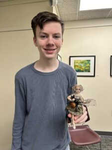 teen boy with grey shirt and brown hair with doll with spider web dress and spider glued to web