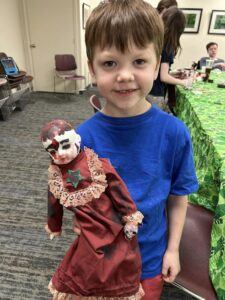 boy with brown hair and blue tshirt with bald doll with bloody head and skull in its hand