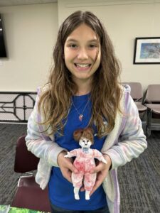 girl with blue shirt and pastel tie dye hoodie and long brown hair with baby doll with bloody clothing and black eyes