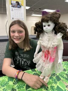 girl with green tshirt and straight brown hair with doll with bloody dress