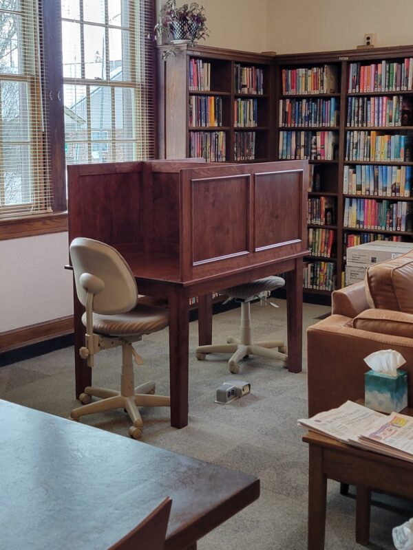 Wooden study carrel, bookshelves, office chair with arms, and window with blinds.