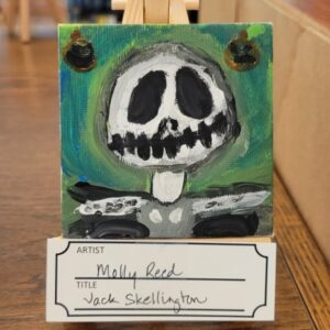 Small painting of a stylized skeleton face on an easel, with green and blue background.