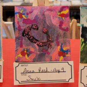 An abstract painting featuring a colorful background and a glittery smiley face.