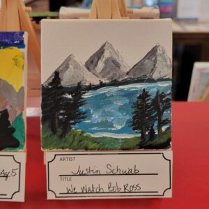 A small landscape painting on an easel depicts mountains, water, and trees.