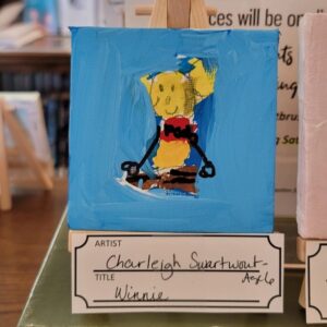 A small abstract painting of a yellow bear on a blue canvas, displayed on an easel.