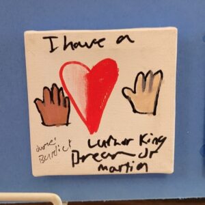 A canvas with a heart flanked by two hands of different skin tones and handwritten text expressing a message of unity.