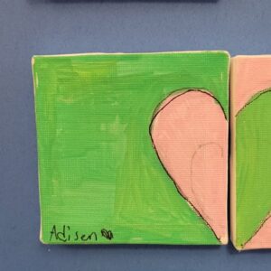 A canvas painting with a large pink half heart shape on a green background, with a signature in the bottom right.