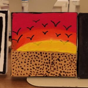 Small canvas painting with a red, orange, and yellow sky, black birds, and a brown landscape with black dots.