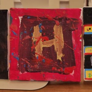A small canvas with a gold letter "H" on a dark background, surrounded by red and blue paint splatters.