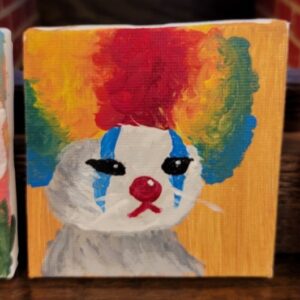 Painting of a clown kitten with a colorful afro and a white face with blue markings.