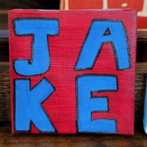 A small canvas with "JAKE" in blue block letters on a red background.