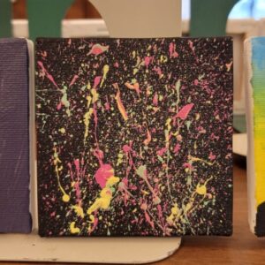 A small canvas with a black background and multicolored paint splatters.
