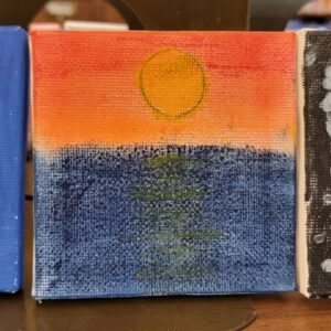 A small painting of a yellow sun over an orange sky above a deep blue body of water.