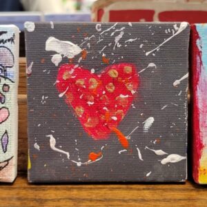 Small painting of a red heart with gold dots on a gray background with white and orange splatters.