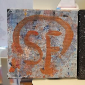 Abstract canvas with "SF" in orange-brown paint over a colorful speckled background.