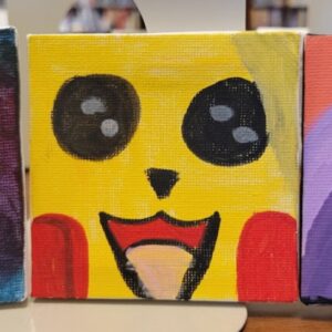 A small canvas painting of a yellow cartoon character with large black eyes, red cheeks, and an open, smiling mouth.