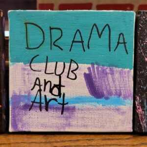 A small canvas painted with "DRAMA CLUB and Art" in black lettering on teal and purple background.