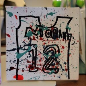 Canvas with abstract paint splatters and a black outline of a jersey with number 12.