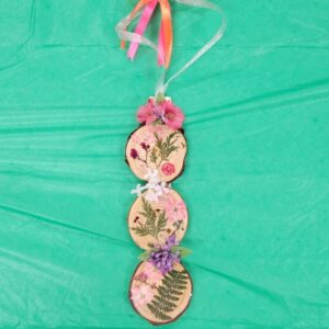 Three wooden slices with pressed flowers on a green background, topped with a colorful bow