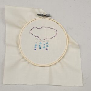 Embroidery of a cloud with beaded raindrops in a hoop on fabric