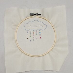Embroidery hoop with a cloud and bead raindrops on fabric