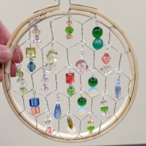 A wooden embroidery hoop with wire mesh and colorful hanging beads